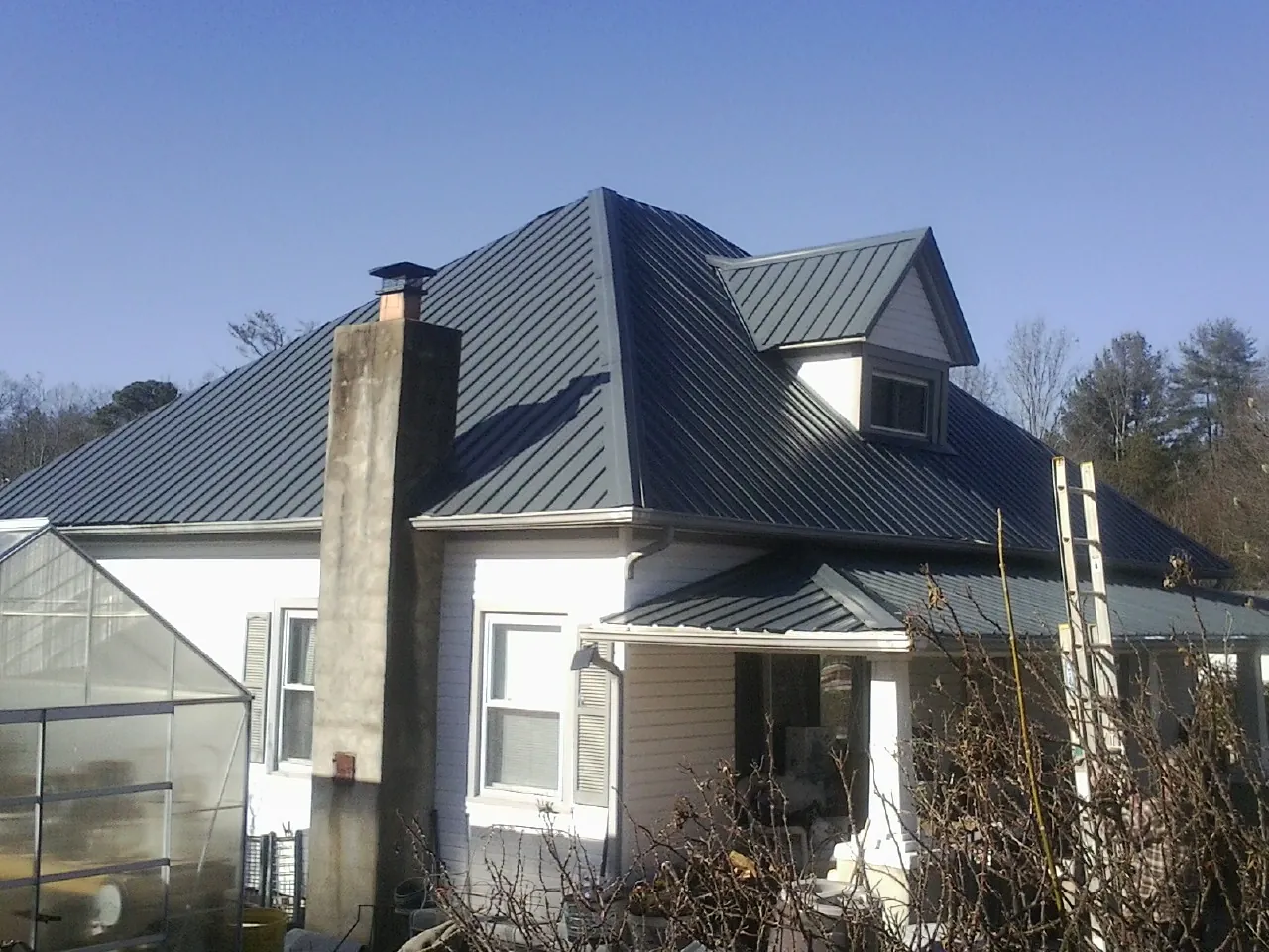 Dark blue standing seam metal roof on a white farmhouse with dormer — Slate & Tile Roof Repair by Roofing Brothers in Camanche