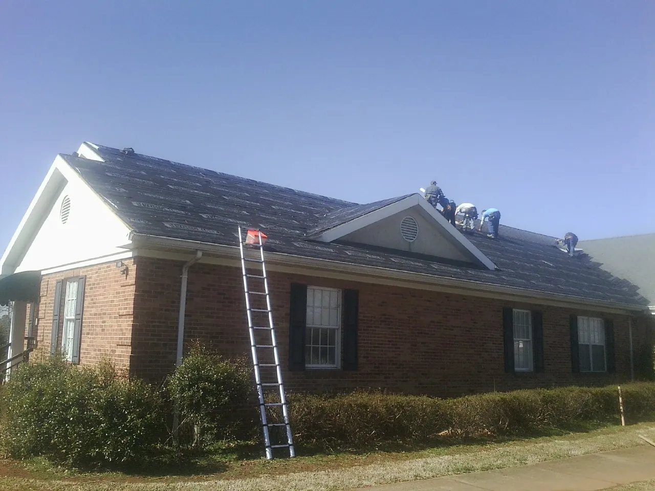 Crew tearing shingles off a brick ranch roof with a ladder set — Emergency Roof Repair work by our crew in Camanche