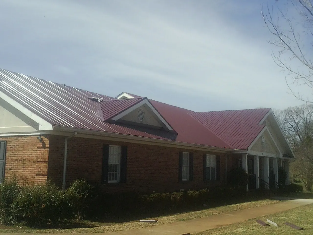 Red metal roof with gabled entries on a long brick building, from a Hail Damage Roof Repair job in Camanche