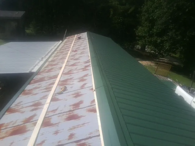 Old rusted panels beside newly installed green metal roofing — Wind Damage Roof Repair by Roofing Brothers in Camanche