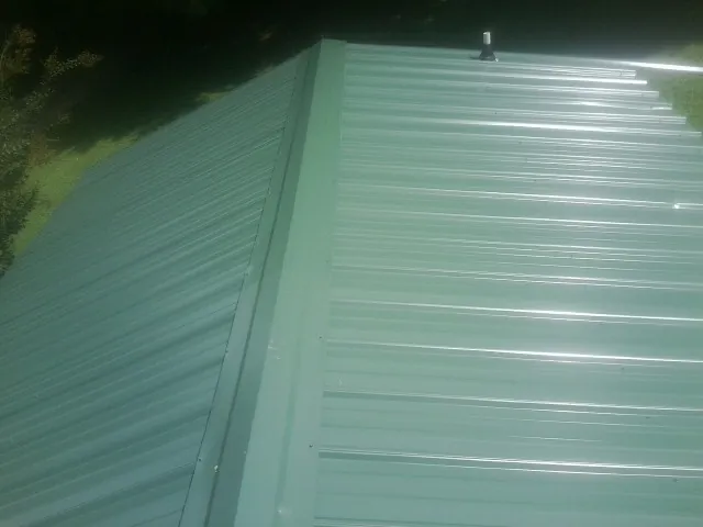 New green metal panels meeting at the ridge of a roof — Flat Roof Repair work by our crew in Camanche