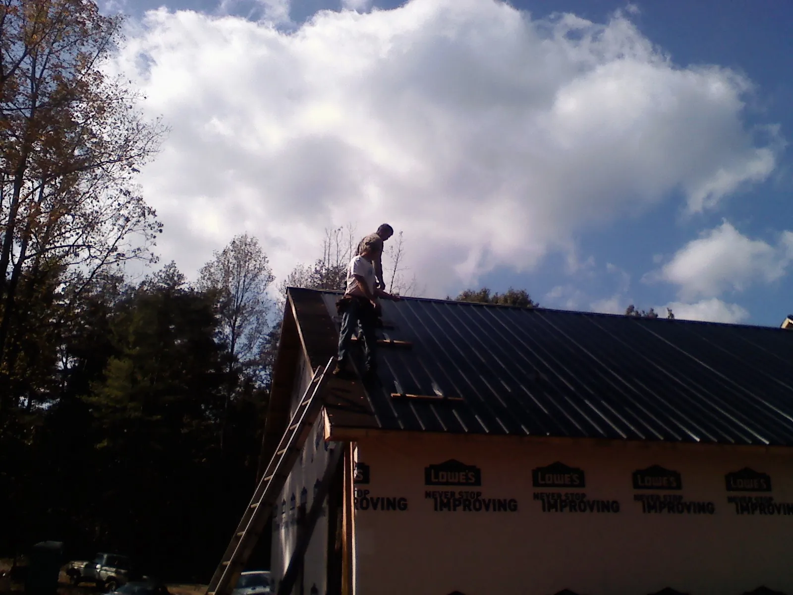 Roofer fastening dark metal panels high against a cloudy sky, from a Roof Inspection job in Camanche