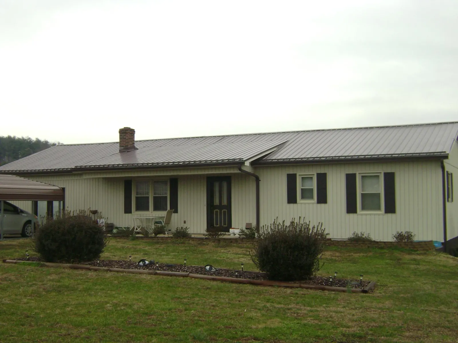 Brown metal roof on a cream sided ranch home with a brick chimney in Camanche