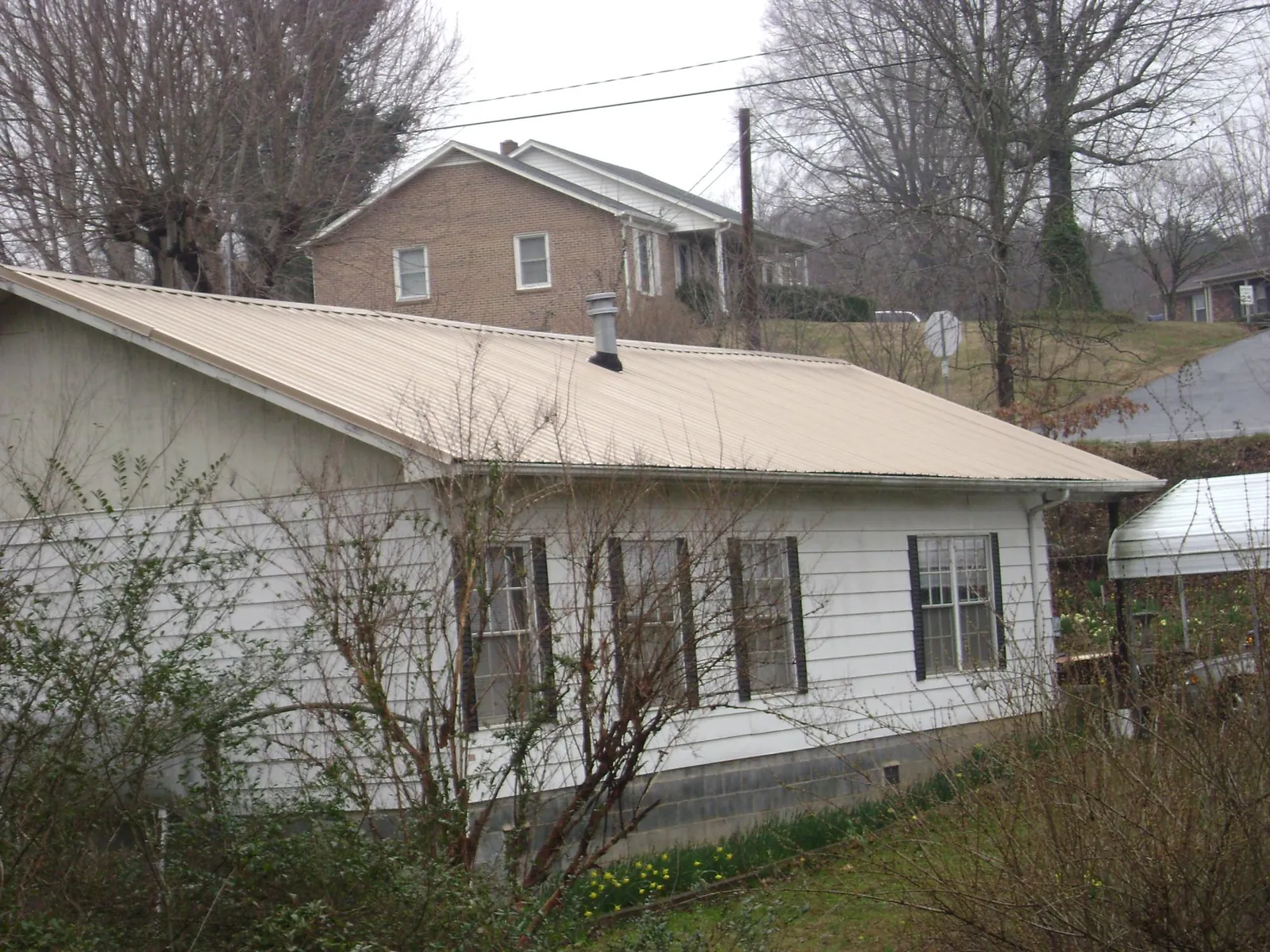 Tan metal roof on a white sided house set into a hillside — Commercial Roofing by Roofing Brothers in Camanche